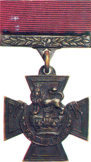The Victoria Cross: a bronze cross pattée bearing a crown surmounted by a lion and the scroll 'For Valour', hanging from a crimson riband